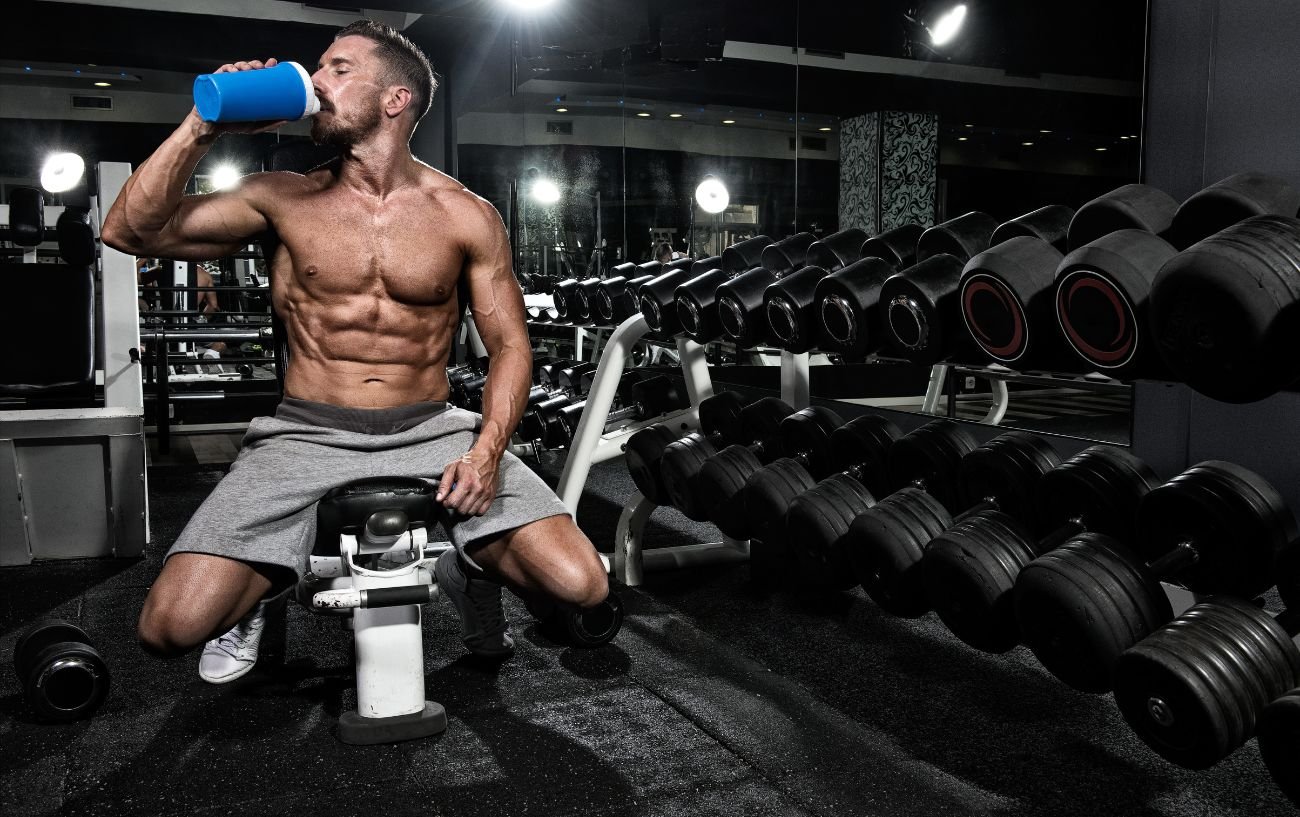 Una persona musculosa bebe un batido de proteínas en el gimnasio.
