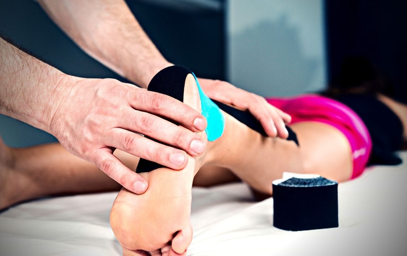 Un fisioterapeuta aplica cinta KT al pie de alguien.