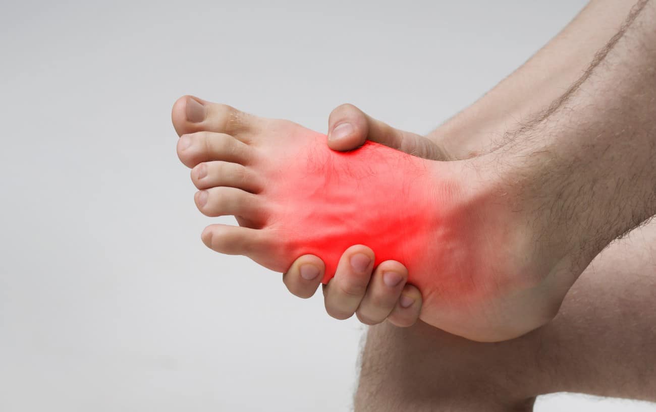 Una persona sosteniendo su pie.  La parte superior del pie está en rojo para mostrar el dolor. 