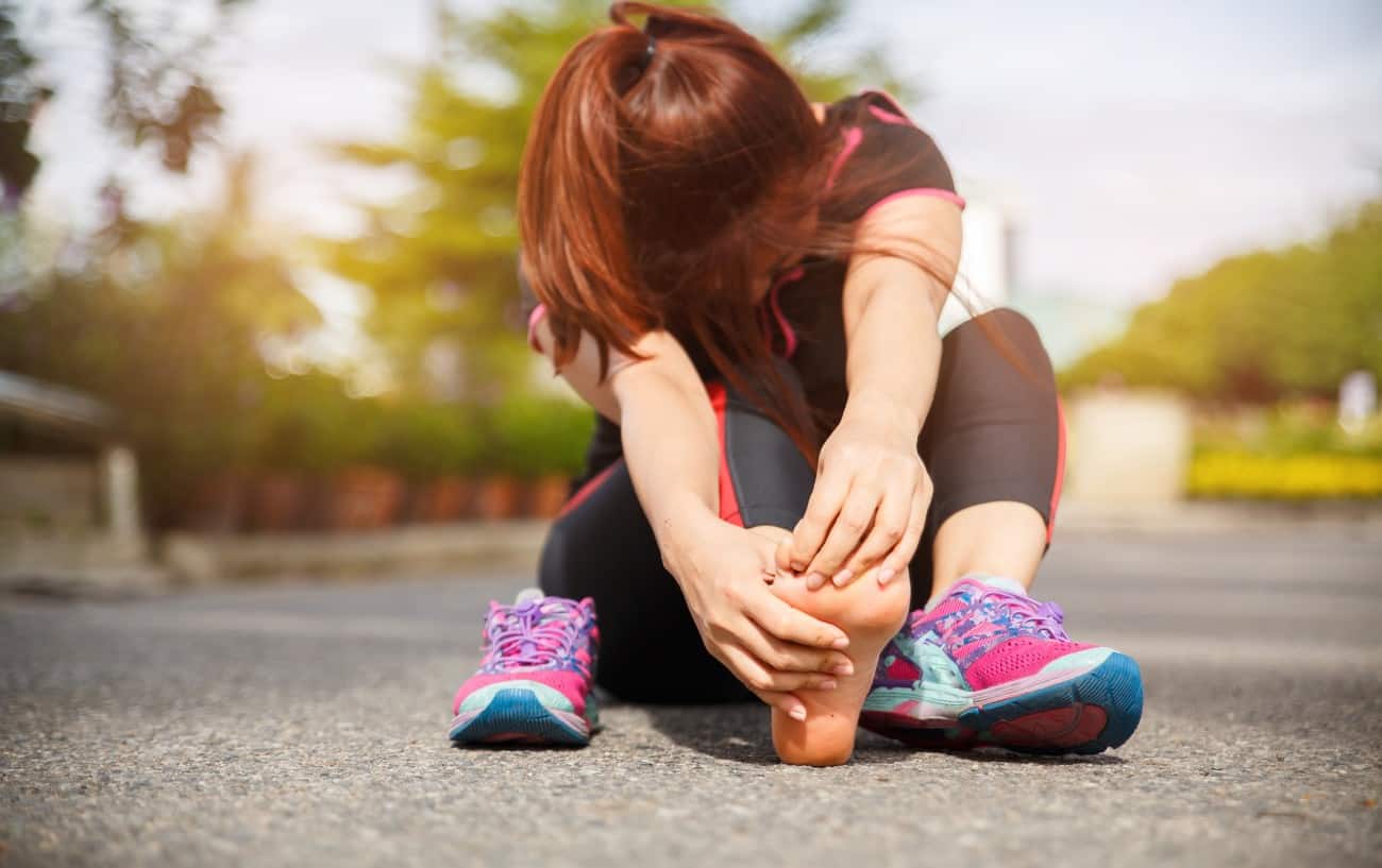 Una mujer en la carretera sujetando su pie debido al dolor en el pie por correr.