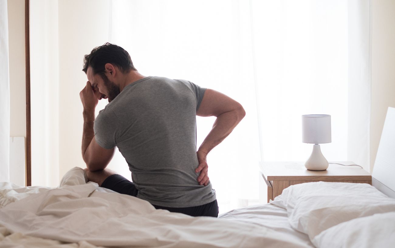 Una persona que se sujeta la espalda con dolor mientras está sentada en la cama.