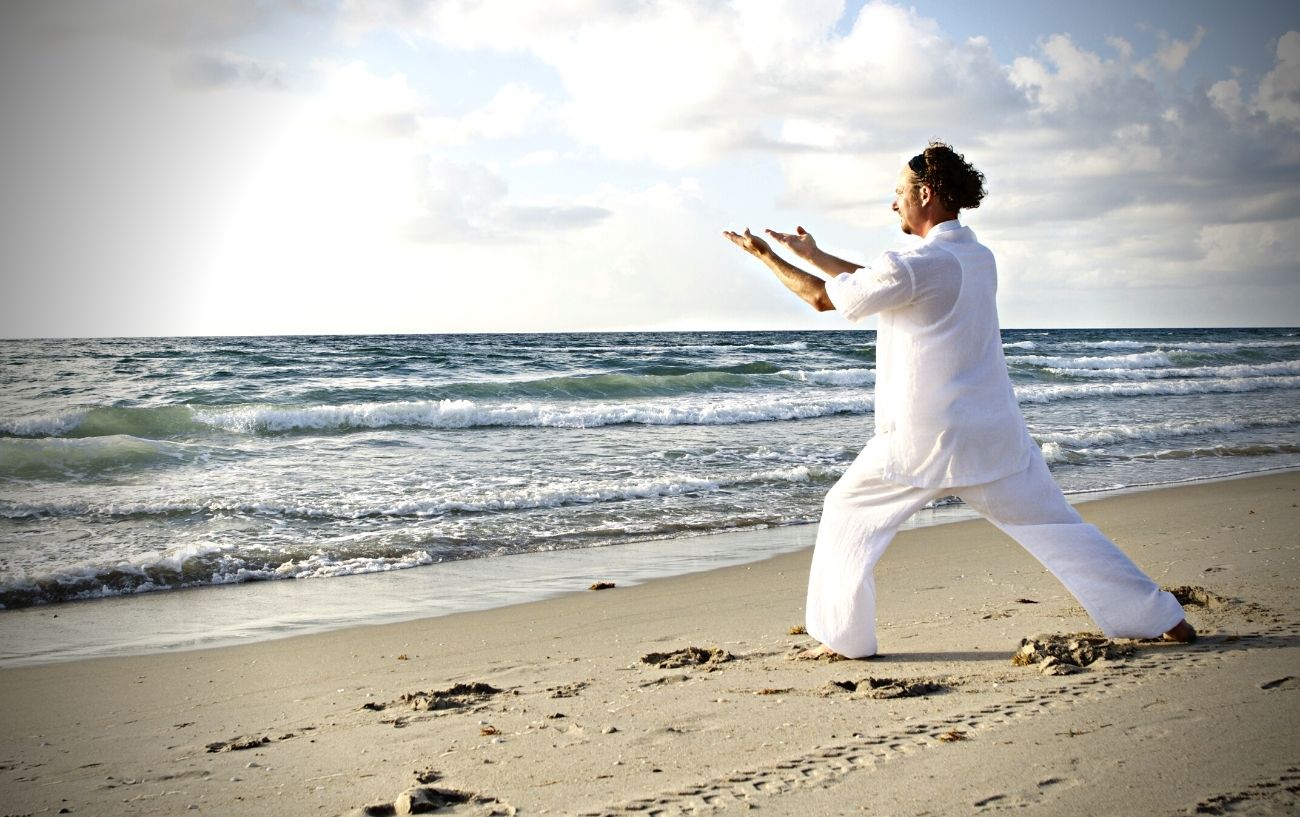 Una persona practicando Tai Chi en una playa.