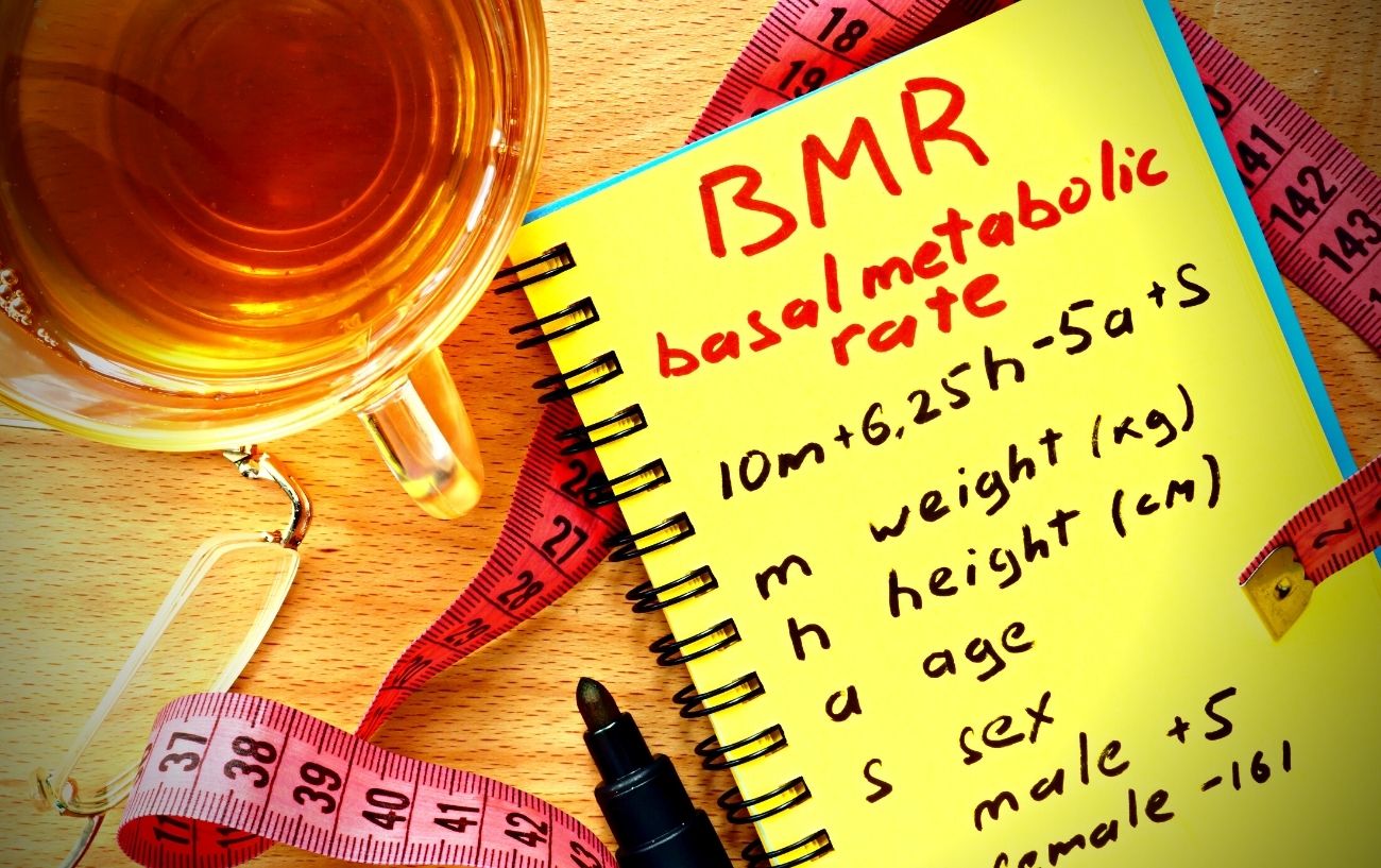 Un cuaderno con notas sobre BMR, una cinta métrica y una taza de té.