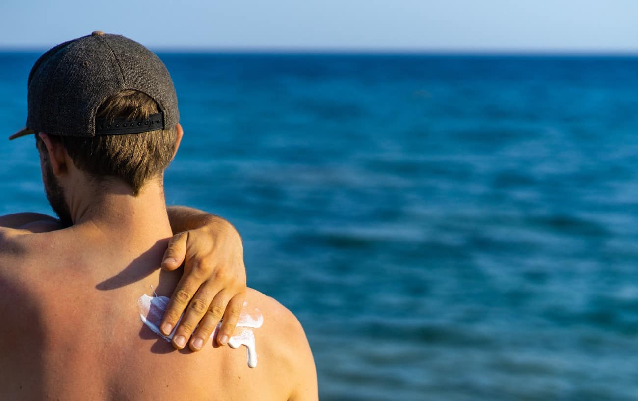 Corredor masculino en la playa se frota protector solar deportivo en la espalda.
