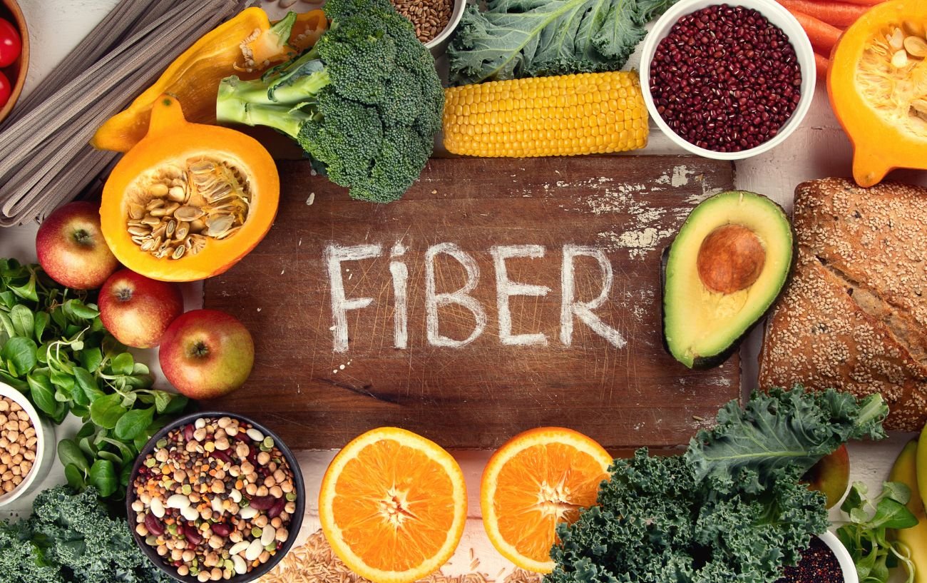 La palabra fibra rodeada de alimentos ricos en fibra como semillas, verduras y frutas.