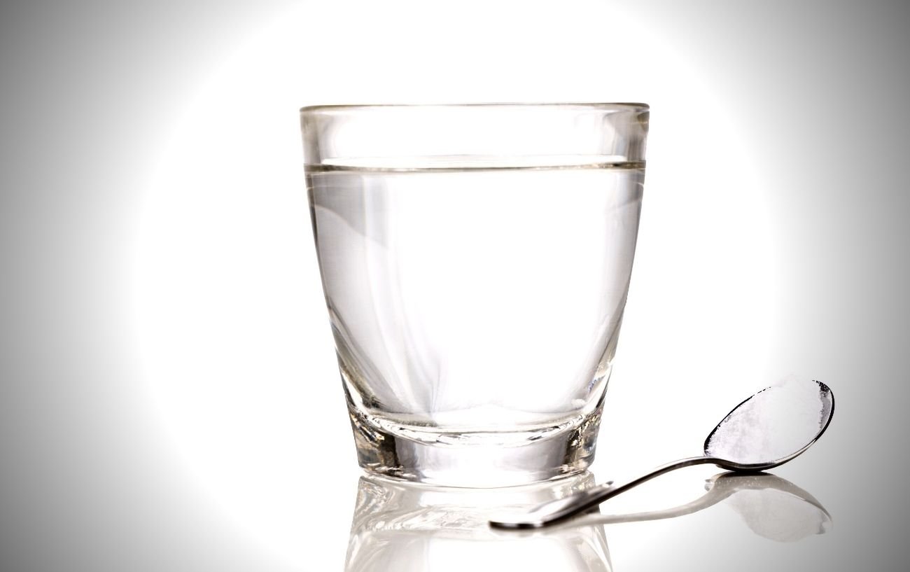 Un vaso de agua con una cucharada de electrolito en polvo al lado. 