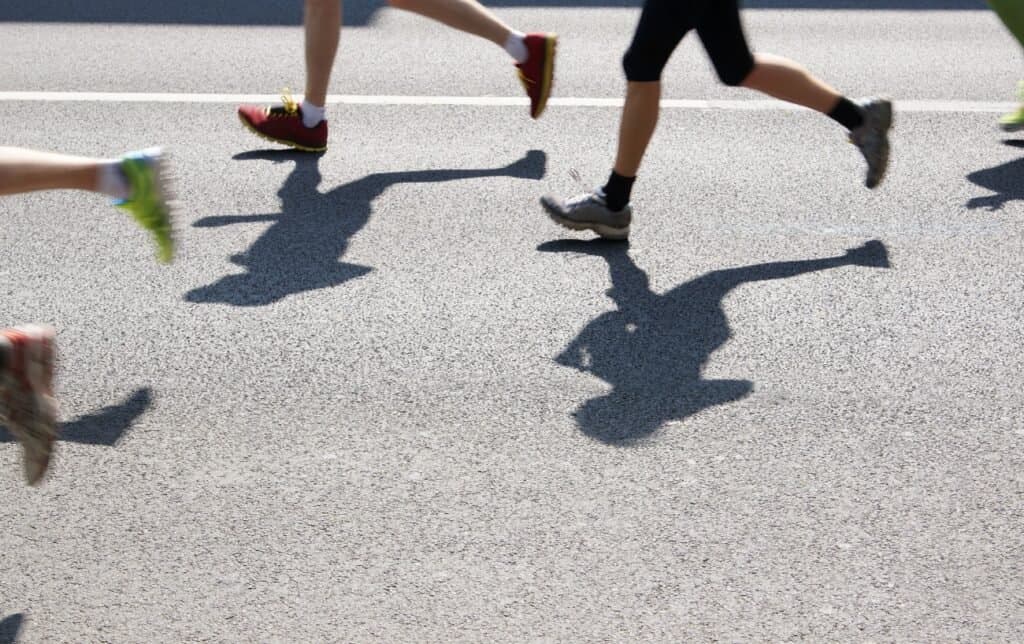 Una imagen de las piernas de los corredores y sus sombras sobre el asfalto