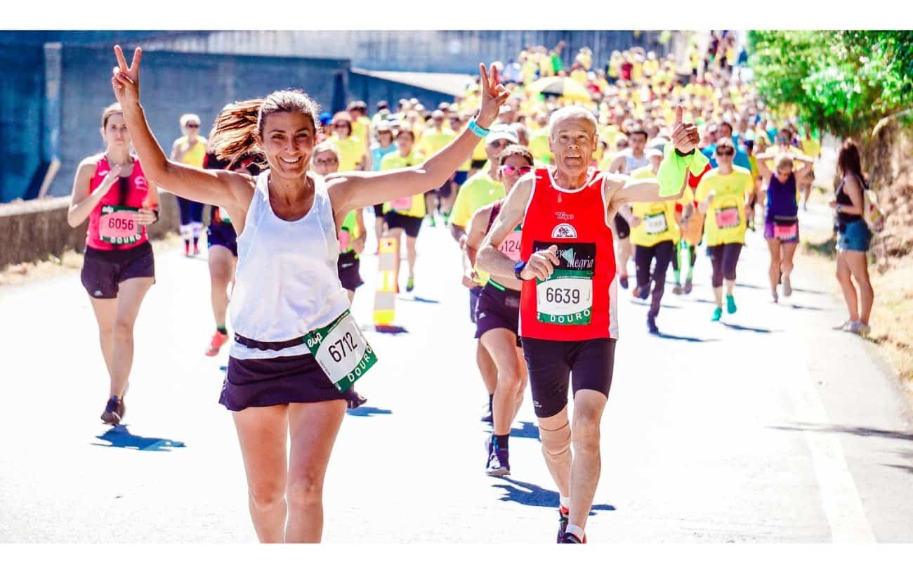 una joven y un hombre ligeramente detrás de ella y a la derecha, ambos luciendo felices durante una carrera de maratón con una multitud de compañeros corredores estirándose detrás de ellos