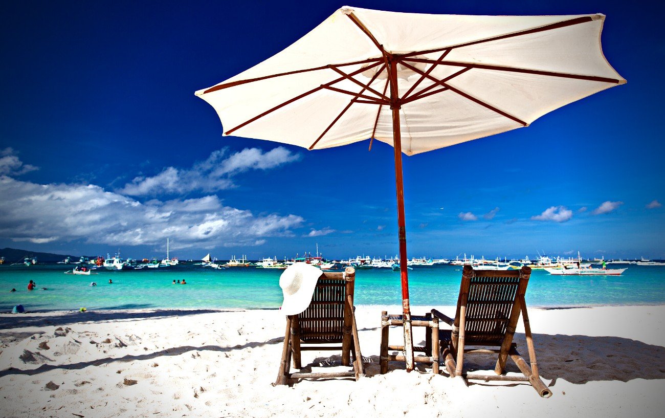 Una escena de playa con sillas, sombrilla y botes.