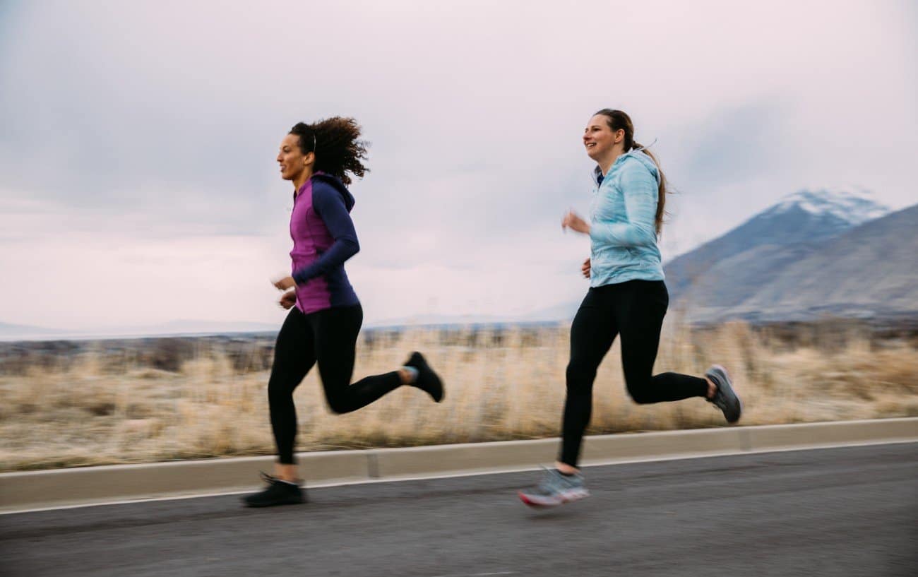 dos mujeres corriendo por una carretera con montañas detrás